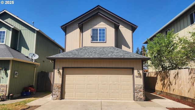 traditional home with concrete driveway, stone siding, a shingled roof, and fence