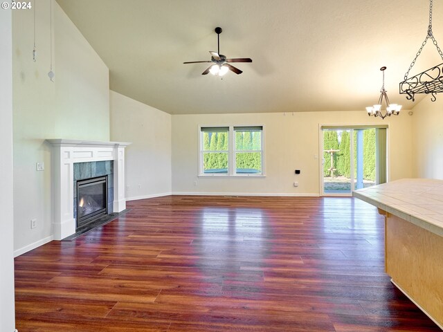 unfurnished living room featuring ceiling fan with notable chandelier, vaulted ceiling, dark wood-type flooring, and plenty of natural light