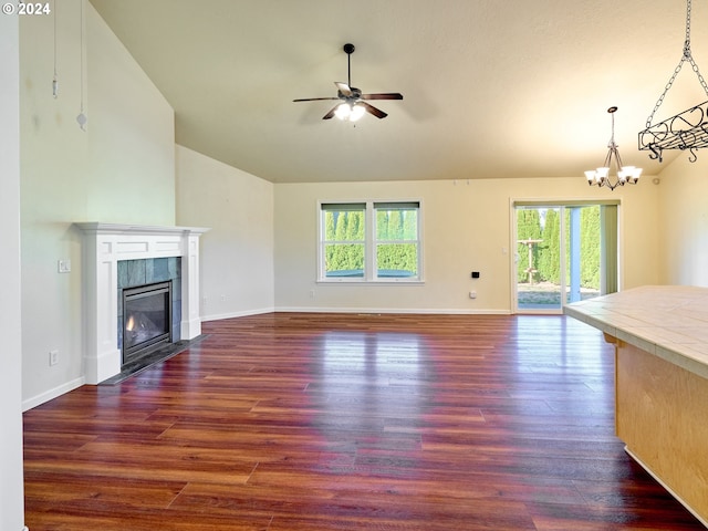 unfurnished living room featuring baseboards, a tiled fireplace, lofted ceiling, dark wood-style flooring, and ceiling fan with notable chandelier