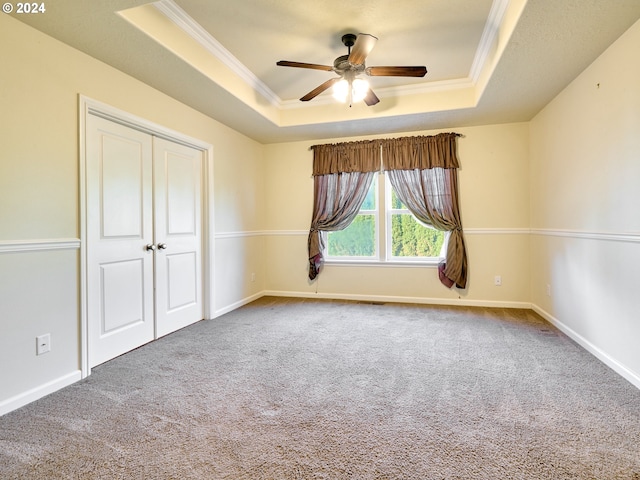 carpeted spare room featuring baseboards, a tray ceiling, ceiling fan, and crown molding