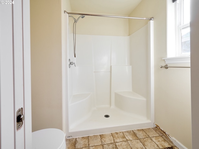 bathroom featuring toilet, stone finish floor, and a shower