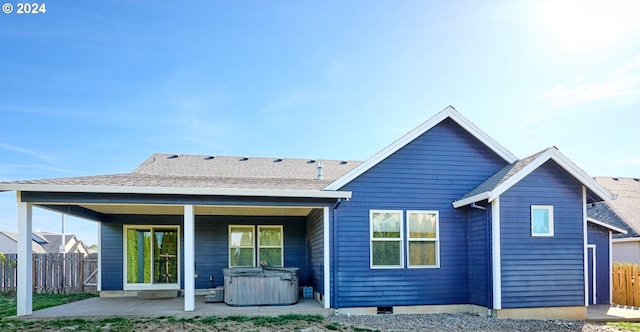 rear view of house with a shingled roof, a patio area, fence, and a hot tub