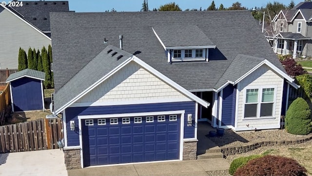 view of front of home featuring roof with shingles, concrete driveway, an attached garage, fence, and stone siding