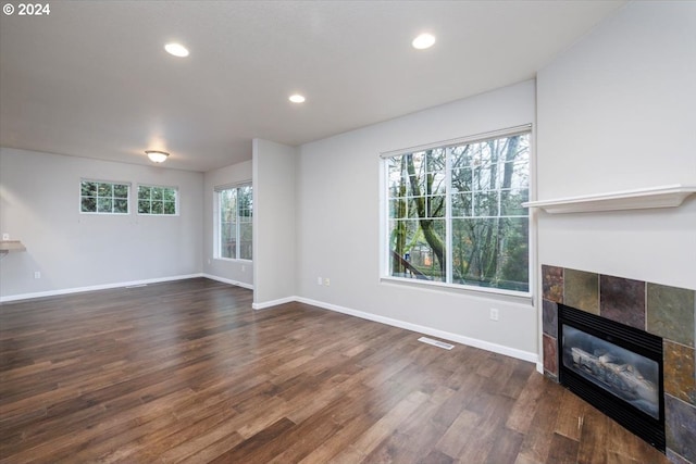 unfurnished living room featuring a tiled fireplace and dark hardwood / wood-style floors