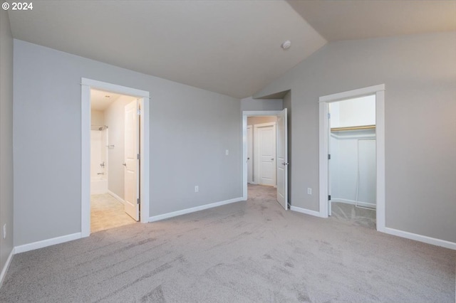 unfurnished bedroom with connected bathroom, light colored carpet, vaulted ceiling, and a closet