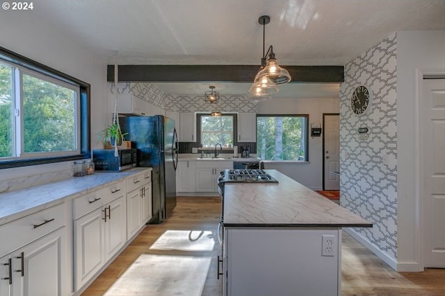 kitchen featuring stainless steel microwave, a center island, freestanding refrigerator, light wood-style floors, and a sink