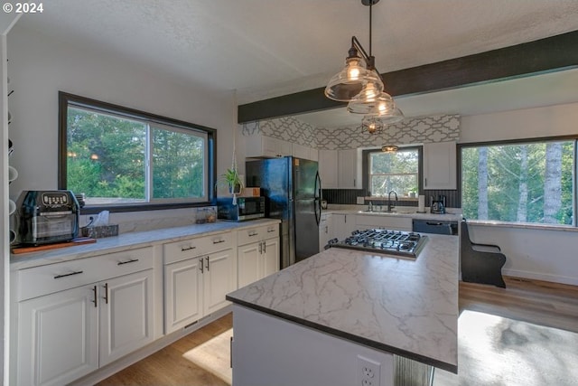 kitchen with black appliances, a kitchen island, light wood-style flooring, white cabinetry, and a sink