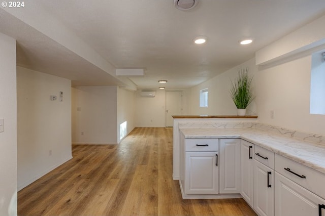 kitchen with white cabinets, a peninsula, light wood-type flooring, and a wall unit AC