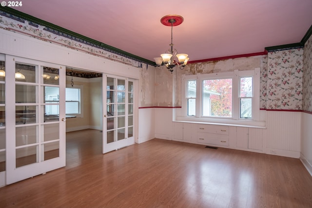 unfurnished dining area with a chandelier, french doors, wainscoting, and wood finished floors