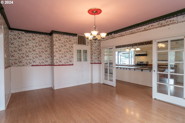 unfurnished dining area with a wainscoted wall, french doors, light wood-style flooring, and an inviting chandelier