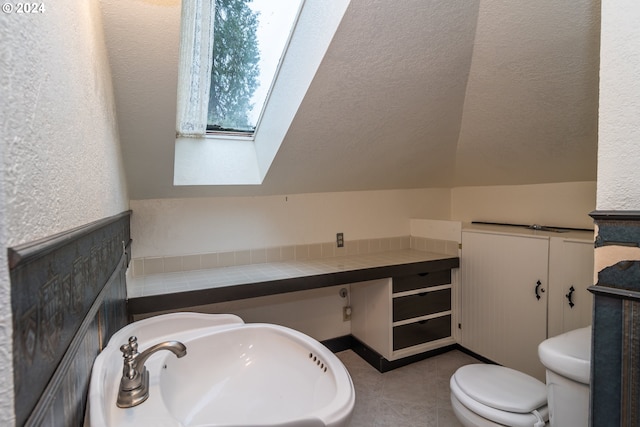 bathroom featuring toilet, lofted ceiling with skylight, tile patterned floors, a textured ceiling, and a sink