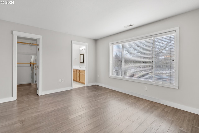 unfurnished bedroom with a closet, ensuite bath, a walk in closet, and light hardwood / wood-style flooring