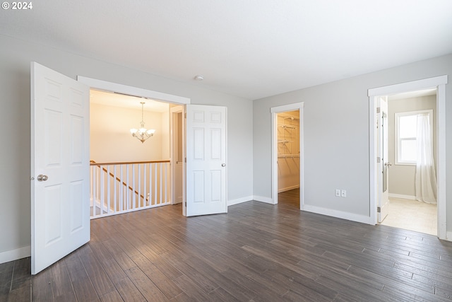 unfurnished bedroom featuring a walk in closet, a chandelier, a closet, and dark wood-type flooring