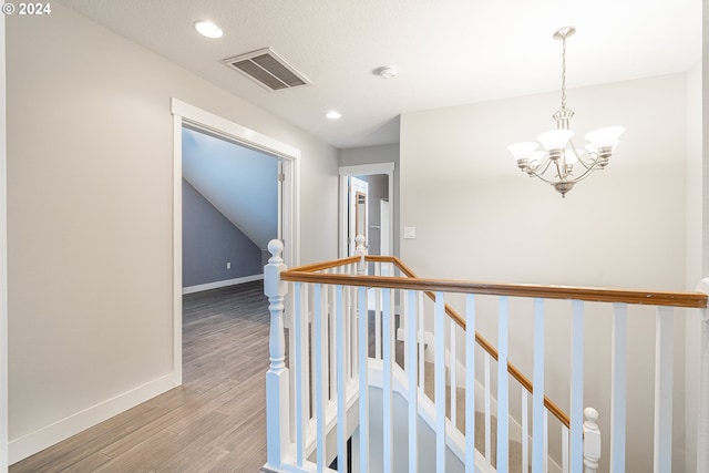 hallway featuring wood-type flooring, a textured ceiling, and an inviting chandelier