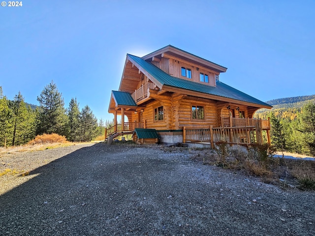 view of front of home featuring log exterior, a view of trees, covered porch, and metal roof