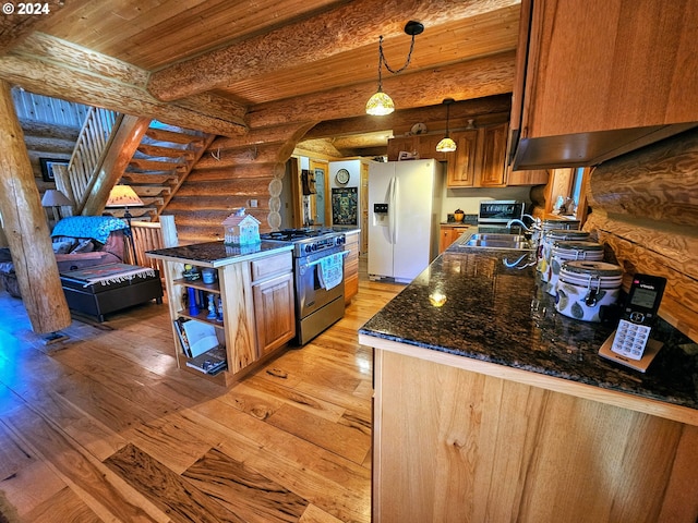 kitchen with stainless steel range with gas cooktop, dark stone countertops, white refrigerator with ice dispenser, rustic walls, and light wood-style floors