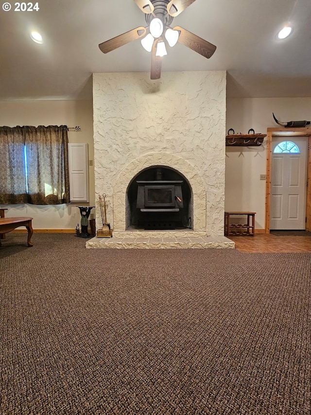 unfurnished living room featuring a wood stove, carpet flooring, and ceiling fan