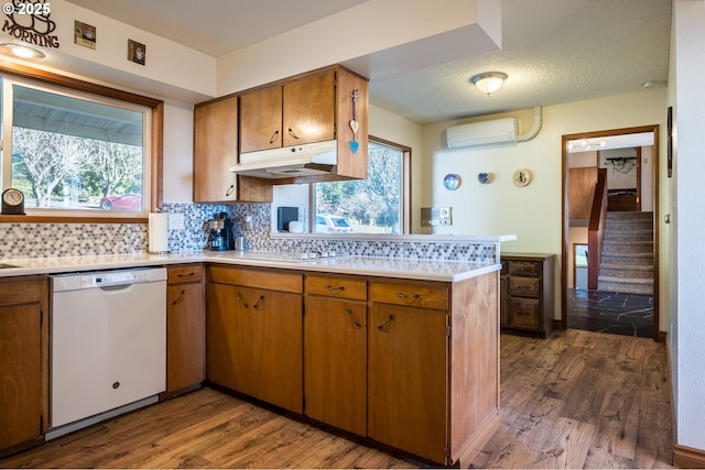 kitchen with tasteful backsplash, white dishwasher, a wall unit AC, a healthy amount of sunlight, and dark hardwood / wood-style floors