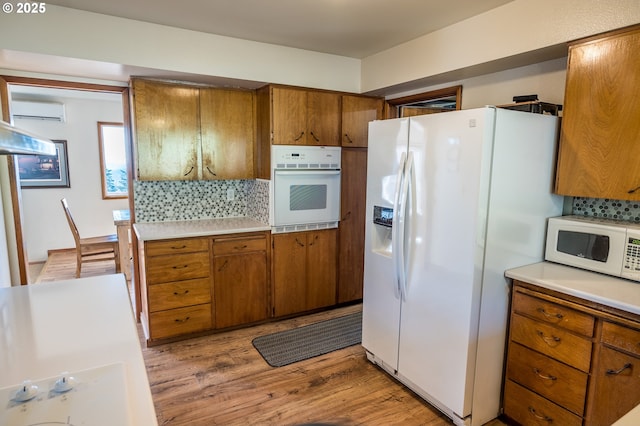 kitchen with white appliances, light hardwood / wood-style flooring, an AC wall unit, and tasteful backsplash