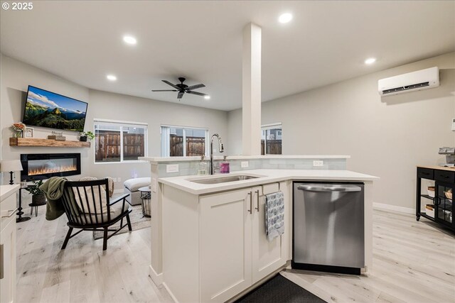 kitchen featuring light countertops, stainless steel dishwasher, an AC wall unit, white cabinets, and a sink