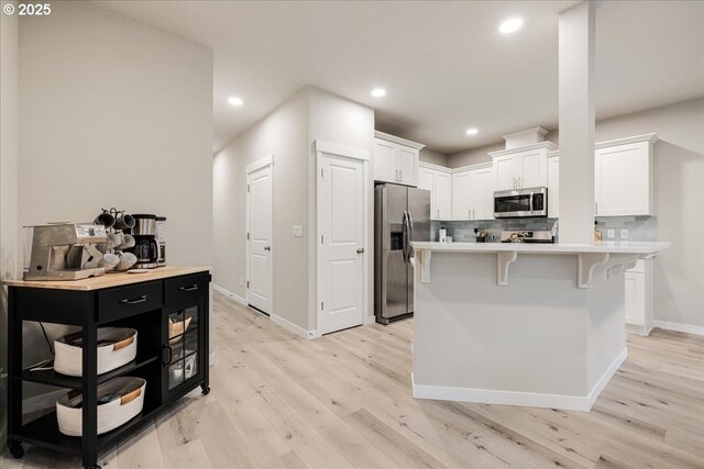 kitchen with a kitchen island, white cabinetry, light countertops, appliances with stainless steel finishes, and a kitchen bar