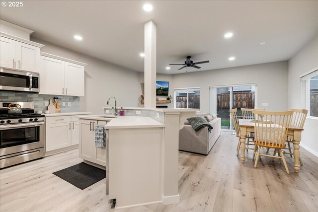 kitchen featuring open floor plan, stainless steel appliances, light countertops, white cabinetry, and a sink