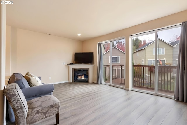 living area featuring a glass covered fireplace, recessed lighting, wood finished floors, and baseboards