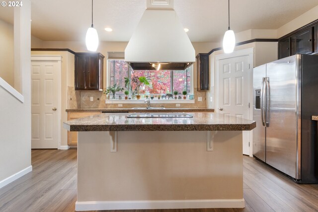 kitchen featuring custom exhaust hood, stainless steel fridge, dark brown cabinetry, and light wood-type flooring