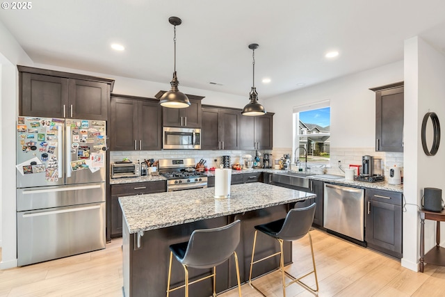 kitchen with appliances with stainless steel finishes, a sink, a kitchen island, dark brown cabinets, and light wood-type flooring