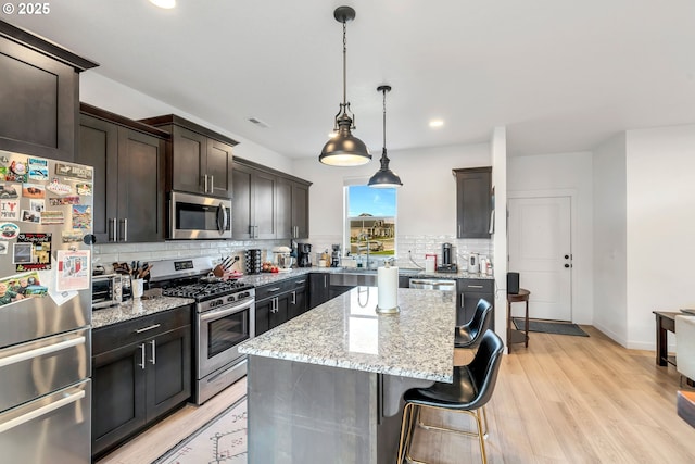 kitchen with light stone counters, a kitchen breakfast bar, appliances with stainless steel finishes, light wood-type flooring, and tasteful backsplash