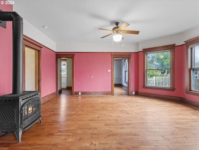 unfurnished living room with a wood stove, ceiling fan, and light hardwood / wood-style floors