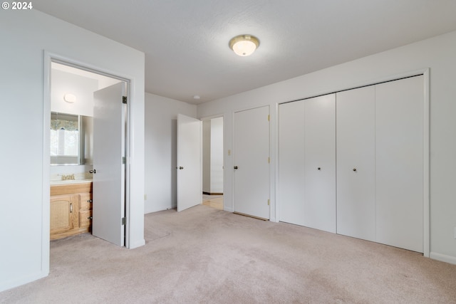 unfurnished bedroom featuring a closet, ensuite bathroom, and light colored carpet