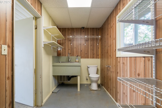 bathroom featuring toilet, a drop ceiling, wooden walls, and concrete flooring