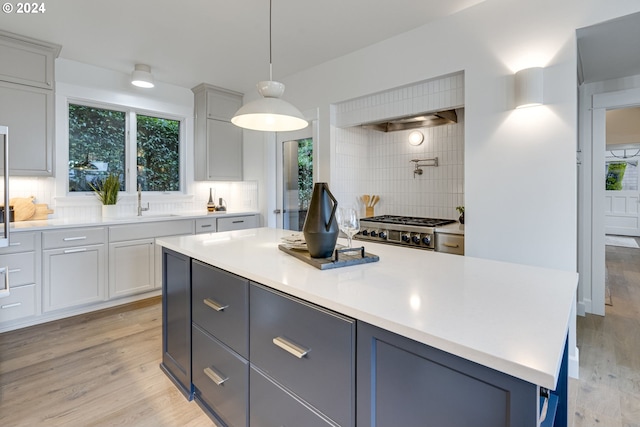 kitchen featuring pendant lighting, sink, backsplash, and light hardwood / wood-style flooring