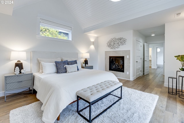 bedroom with a tiled fireplace, lofted ceiling, wooden ceiling, and light hardwood / wood-style floors