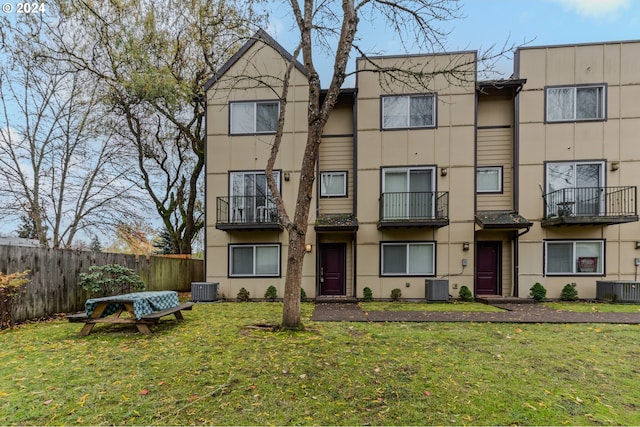 multi unit property featuring central air condition unit, a front lawn, and fence