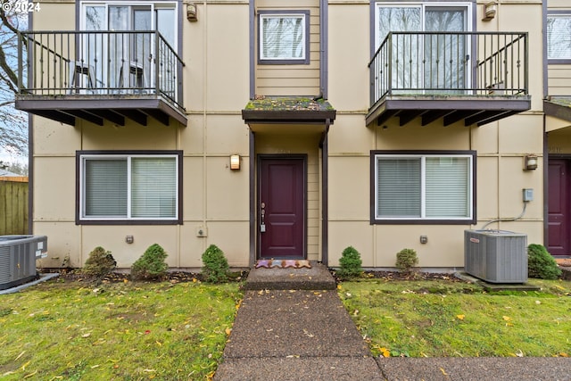 property entrance with a balcony, a yard, central AC unit, and stucco siding