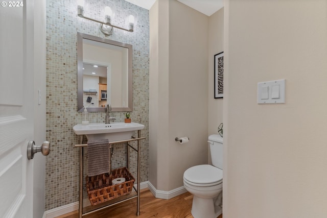 half bathroom with a sink, baseboards, toilet, and wood finished floors