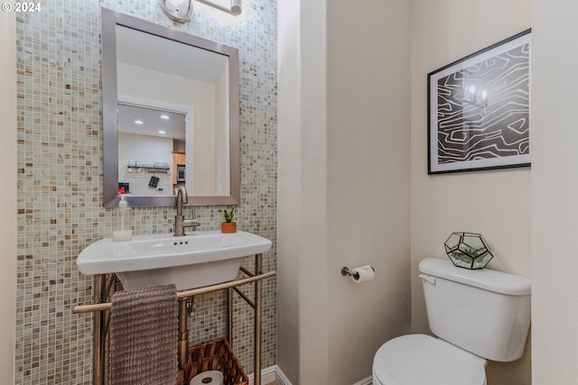 half bathroom featuring toilet, tile walls, and a sink