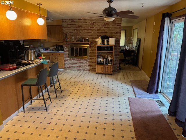 kitchen featuring ceiling fan, decorative light fixtures, a kitchen breakfast bar, and brick wall