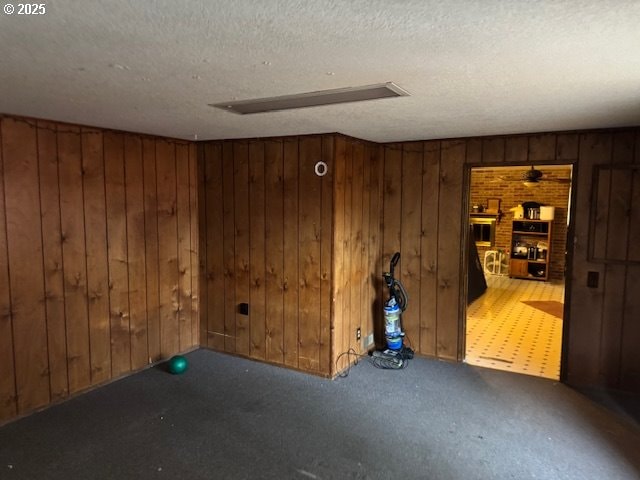 unfurnished room with carpet, wooden walls, and a textured ceiling