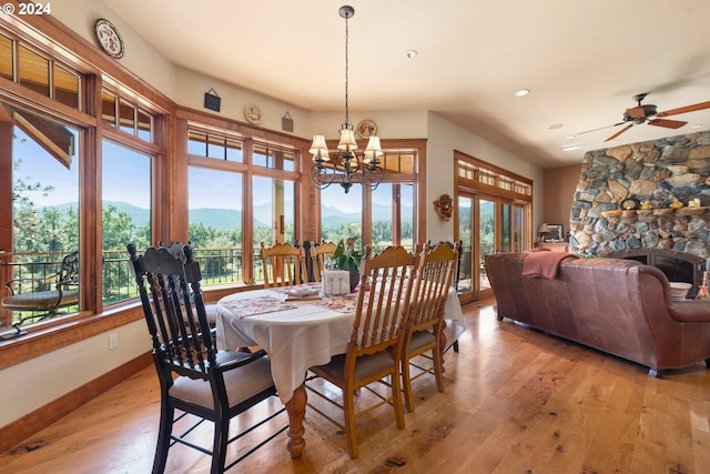 dining room with light hardwood / wood-style floors, ceiling fan with notable chandelier, a fireplace, and a mountain view