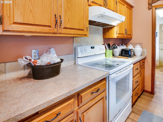 kitchen featuring light wood-type flooring, white electric range, and backsplash