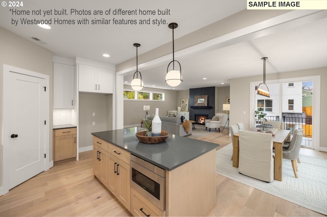 kitchen featuring stainless steel microwave, backsplash, hanging light fixtures, light hardwood / wood-style flooring, and a large fireplace