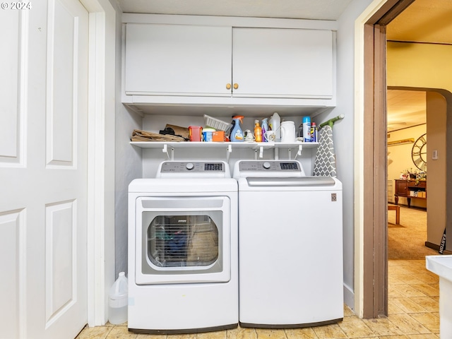 clothes washing area with washer and clothes dryer, cabinets, and light carpet