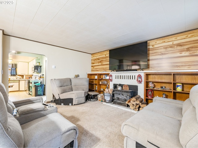 living room featuring carpet, a wood stove, crown molding, and wood walls