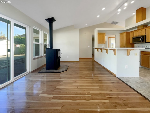 kitchen featuring a wood stove, light wood-type flooring, vaulted ceiling, and a breakfast bar