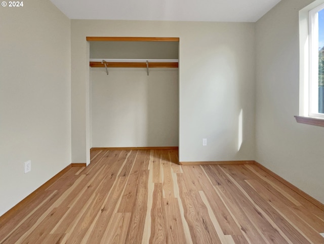 unfurnished bedroom with a closet, light wood-type flooring, and multiple windows