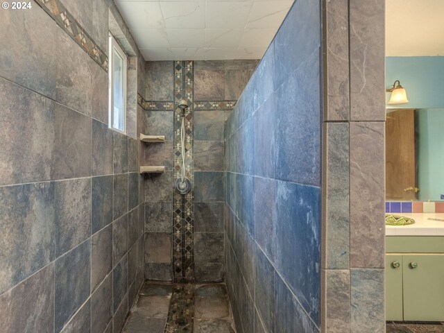 bathroom with tiled shower, vanity, and tile walls