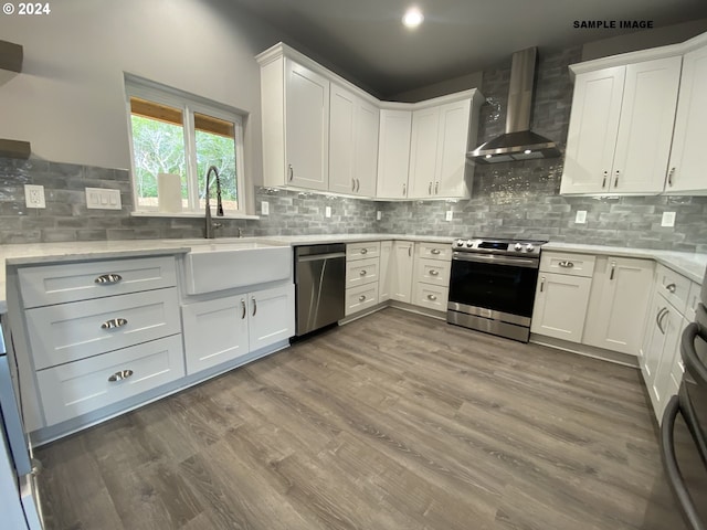 kitchen with wood-type flooring, stainless steel appliances, white cabinetry, wall chimney range hood, and decorative backsplash